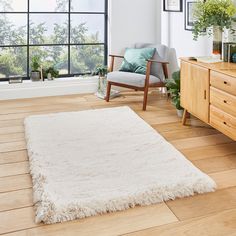 a living room with wooden floors and white rugs on the floor next to a window