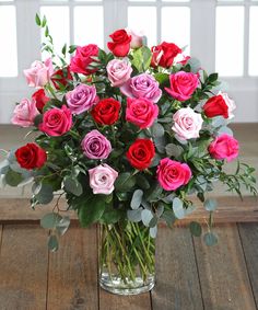 a vase filled with pink, red and purple roses on top of a wooden table