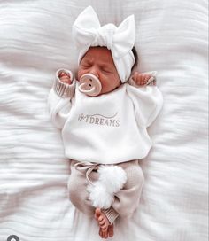 a newborn baby wearing a white outfit with a pacifier in it's mouth