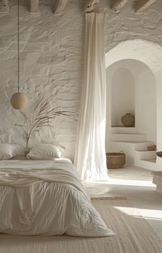 a white bed sitting in a bedroom next to a stone wall covered in drapes