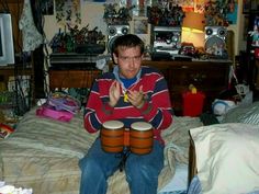 a man sitting on top of a bed holding two drums