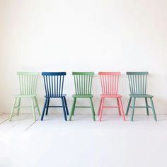 four different colored chairs sitting side by side in a row against a white wall and floor