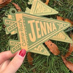 someone holding up a sticker that says jennya on it in front of some leaves