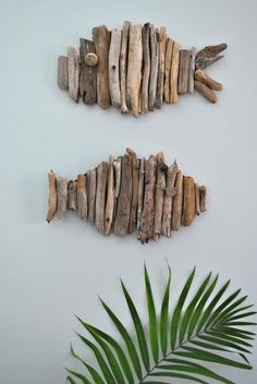 two fish made out of driftwood sitting on top of a wall next to a plant