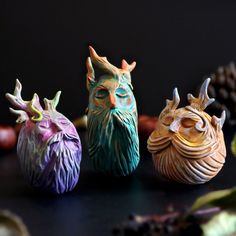 three ceramic owl figurines sitting next to each other on a black surface with pine cones in the background