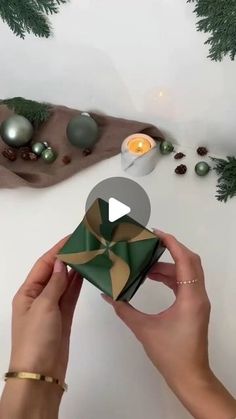 someone holding a present in front of christmas decorations and candles on a white countertop