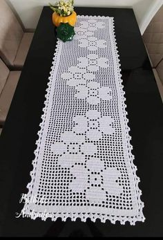 a black table with white crocheted doily next to a vase filled with flowers