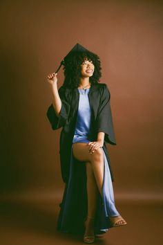 a woman sitting on top of a chair wearing a graduation gown and holding an umbrella