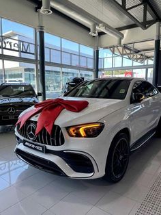 a white mercedes suv with a red bow on it's hood in a showroom