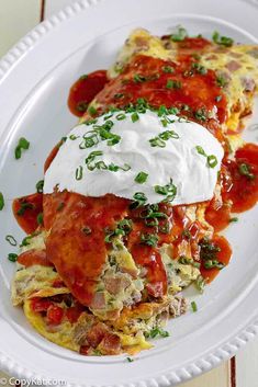 two enchiladas on a white plate with sour cream