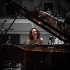 a woman sitting at a piano in front of a man with an orchestra behind her