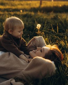 a woman laying in the grass with a child on her lap and looking at each other