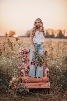 a woman standing on top of an old chair in a field with wildflowers