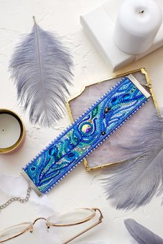 an assortment of feathers and other items on a white surface with a candle, eyeglasses, paperweights, and scissors