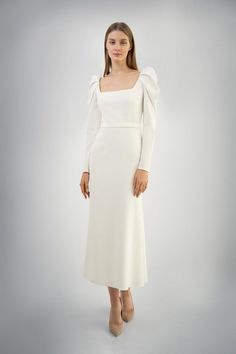 a woman is wearing a white dress with long sleeves and a bow at the neck