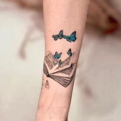 a woman's arm with blue butterflies on top of an open book