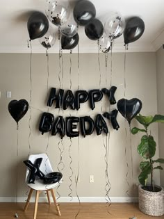 black and white balloons that say happy birthday hanging from the ceiling in front of a chair