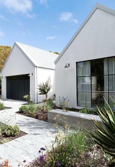 a white house with two garages and plants in the front yard, on a sunny day