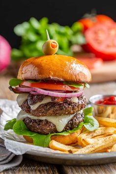 a cheeseburger with onion, lettuce and tomato on a plate next to french fries