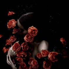 a woman surrounded by red roses in the dark