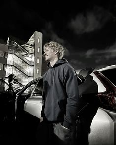 a man standing next to a parked car in front of a tall building at night