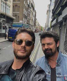 two men standing next to each other on a city street