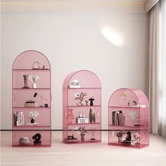 three pink shelves with various items on them in front of a white wall and window