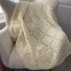 a white crocheted blanket sitting on top of a chair next to a window