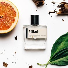 an orange next to a bottle of mukul cologne on a white surface with leaves