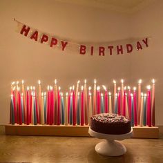 a birthday cake sitting in front of a bunch of lit candles on a table with a banner that says happy birthday