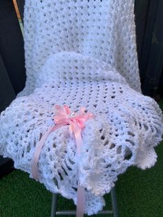 a white crocheted blanket sitting on top of a metal chair with pink ribbon