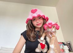 a woman holding a cat wearing a pink hat