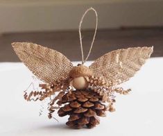 a pine cone angel ornament hanging from a string on top of a table