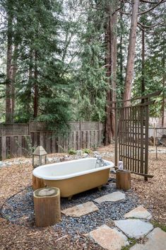 an old bathtub sits in the middle of a graveled area surrounded by trees