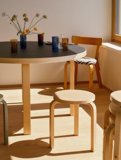 a table with two stools next to it and flowers in vases on the table