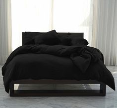 a bed with black sheets and pillows in front of a window