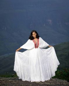 a woman in a white dress standing on top of a hill with her hands on her hips