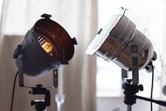 two spotlights on a tripod light in front of a window with white curtains