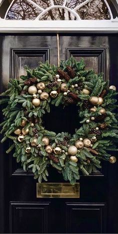 a wreath is hanging on the front door with gold ornaments and pineconis around it