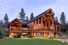 a large wooden house sitting in the middle of a lush green field next to trees