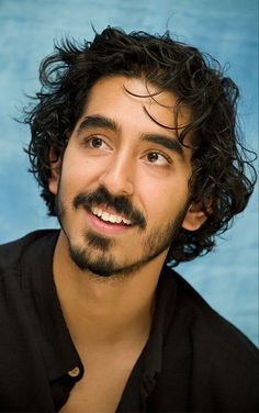 a man with curly hair and a beard smiling at the camera while wearing a black shirt