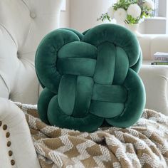 a green knot pillow sitting on top of a white chair next to a blanket and pillows