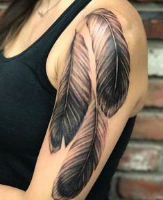 a woman's arm with a black and grey feather tattoo on it