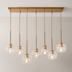 five clear glass globes hanging from a wooden beam in a room with white walls