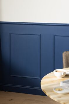 a dining room table with plates and bowls on it, against a blue painted wall