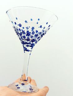 a hand is holding a wine glass with blue flowers on the rim and bottom, in front of a white background