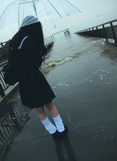 a woman standing in the rain holding an umbrella over her head and looking at the water