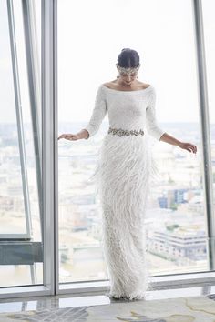 a woman in a long white dress standing next to a window with her arms outstretched