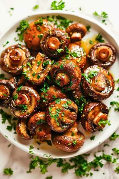 a white plate topped with mushrooms covered in parsley on top of a marble table