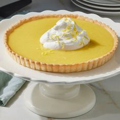 a lemon tart with whipped cream on top sits on a cake plate, ready to be eaten